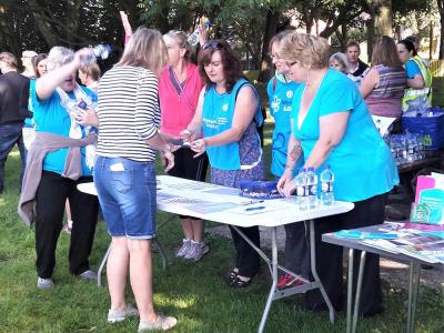 five-women-volunteers-standing-round-table-at-fundraising event-giving-a-woman-information